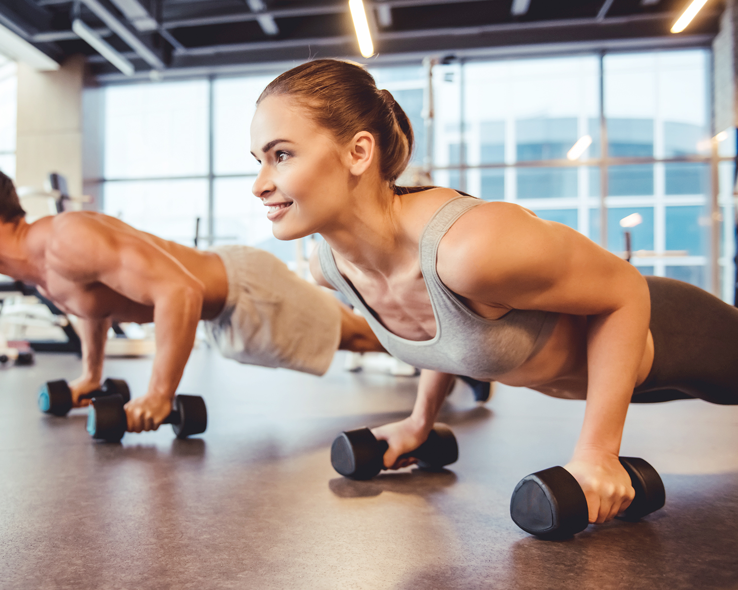 Fit Woman Doing Dumbbell Pushups with Boyfriend at Gym